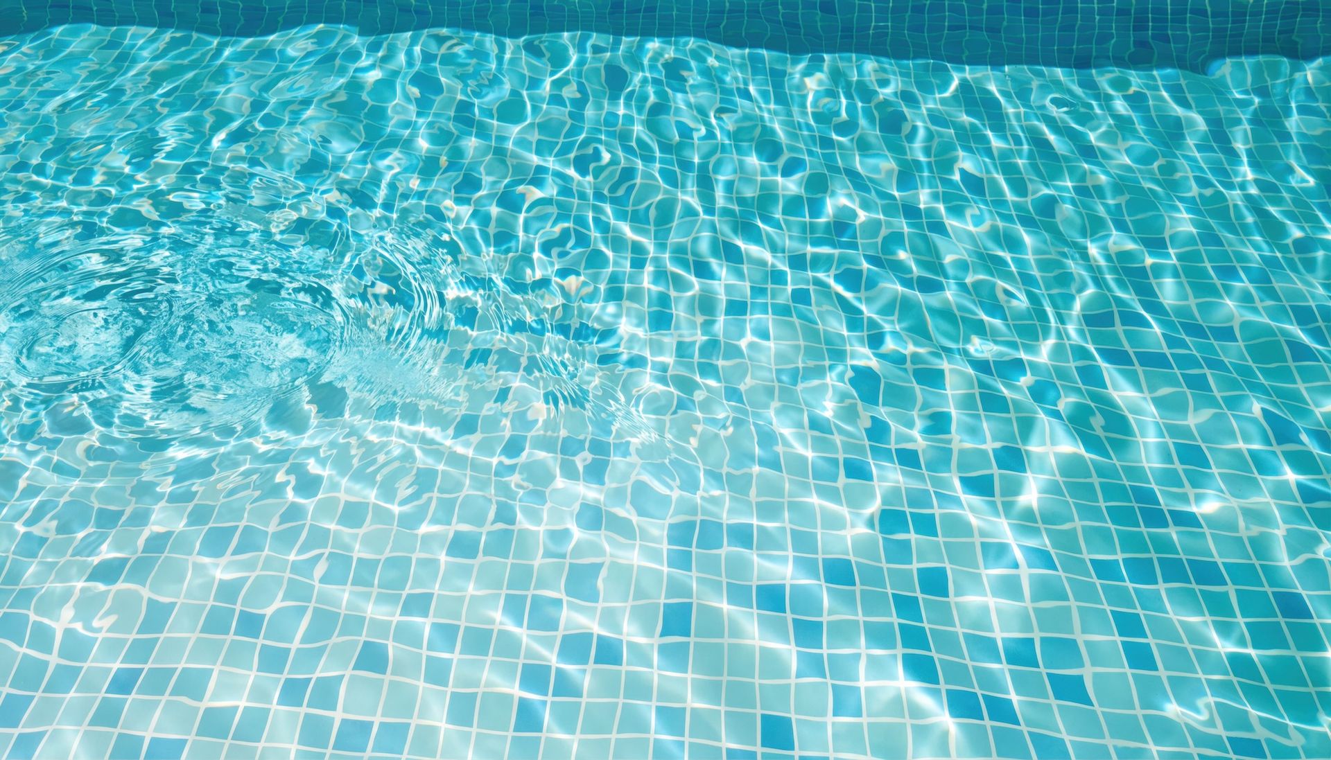 Blue tiled swimming pool water with sunlit ripples and reflections