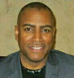 A man in a suit and black shirt is smiling for the camera.