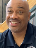 A bald man with a beard is smiling and wearing a black shirt.