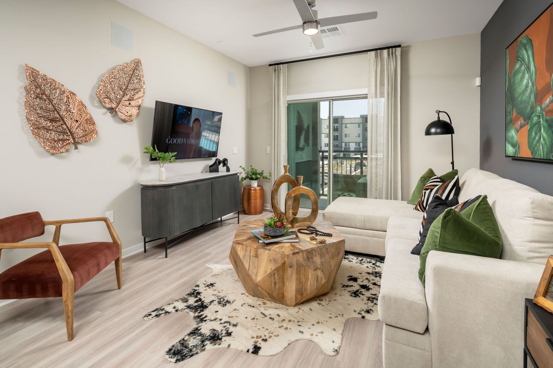 Living room with beige sectional, wooden coffee table, wall-mounted TV, and sliding balcony door.