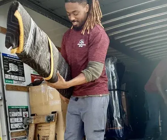 A man with dreadlocks is holding a large piece of furniture in his hands.