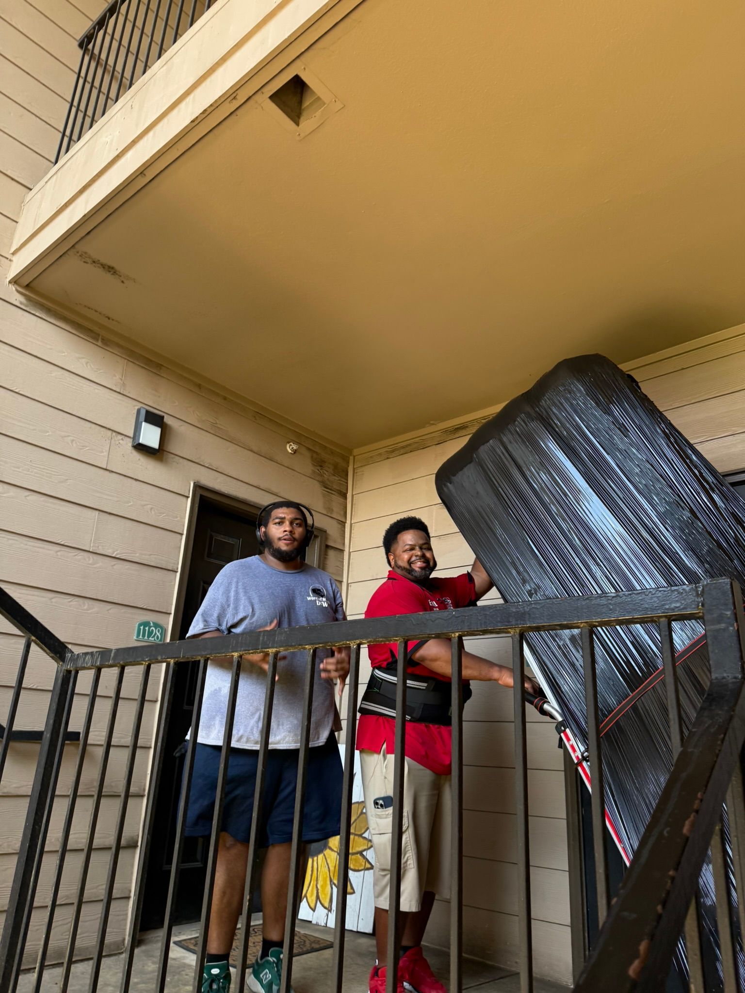 Two men carrying a large, black object up an outdoor staircase of a building.