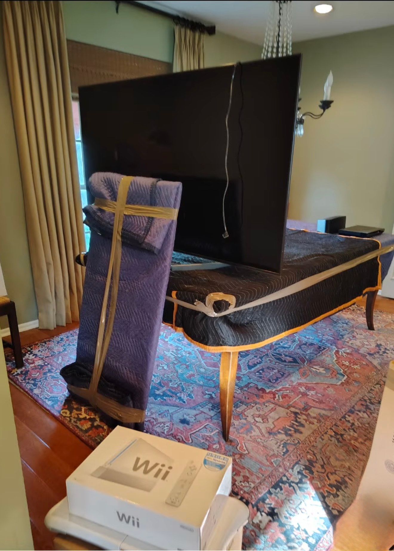 TV and wrapped chair on a piano with a Wii box in front; rug and curtains in background.