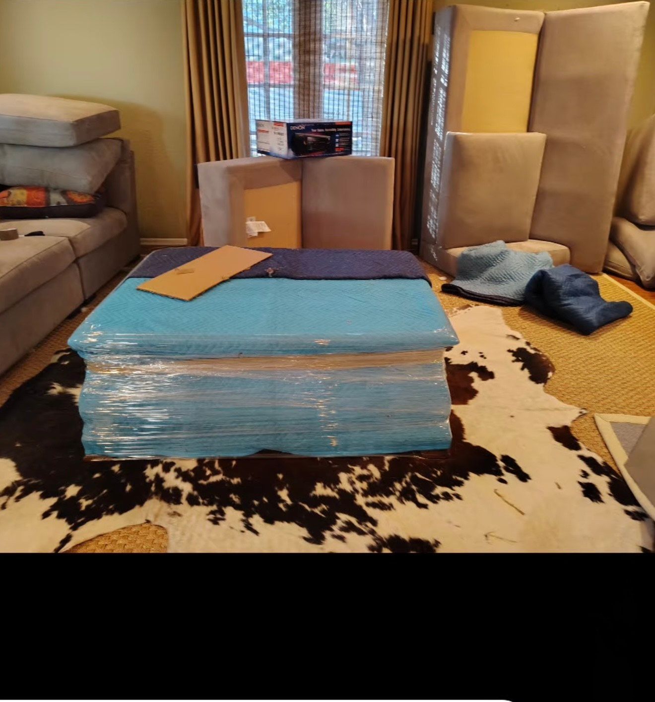 Living room with furniture wrapped for moving, including a large ottoman and sofa.