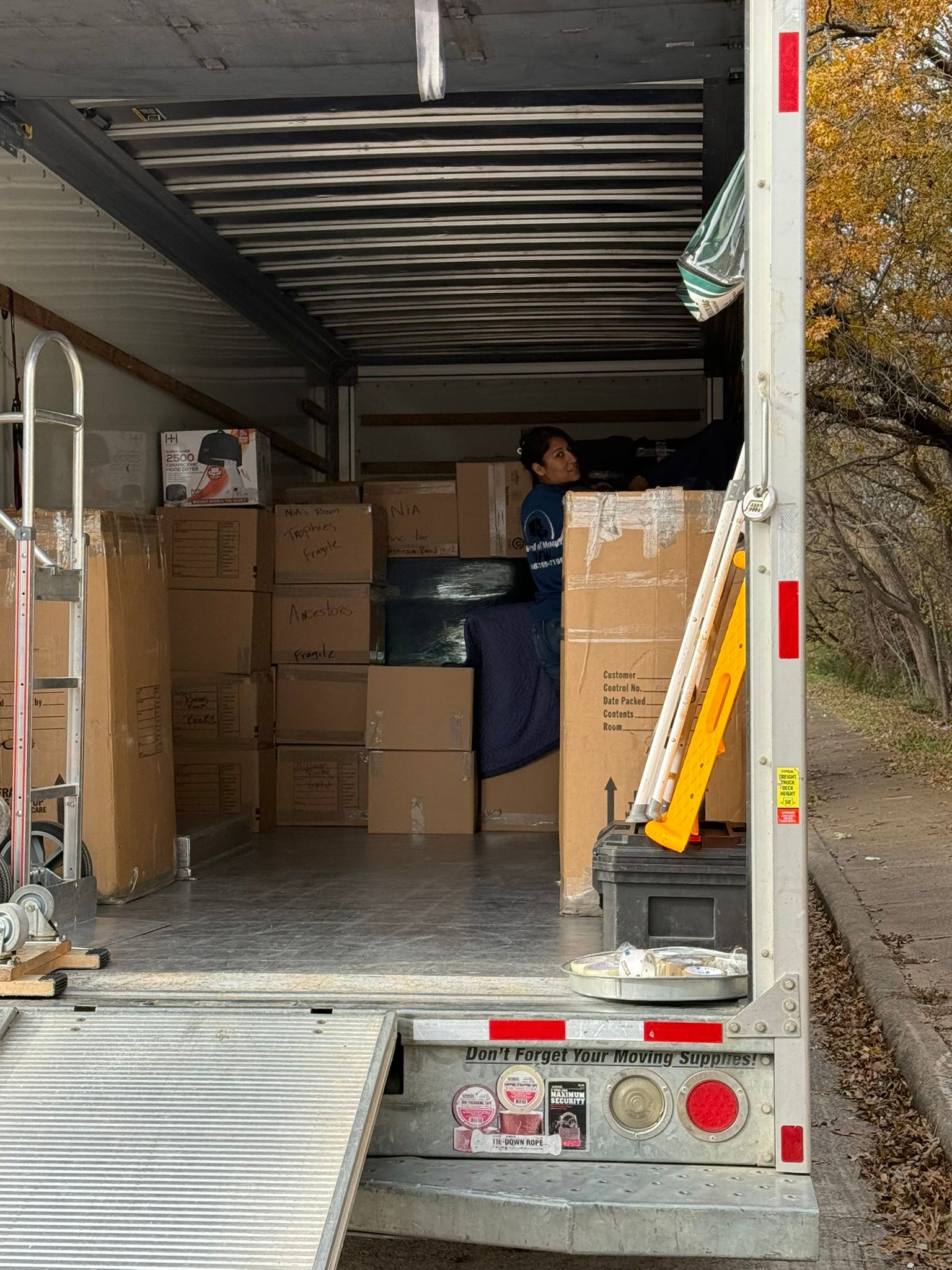 Truck interior loaded with boxes; person in blue shirt inside. Open ramp, side of truck visible.