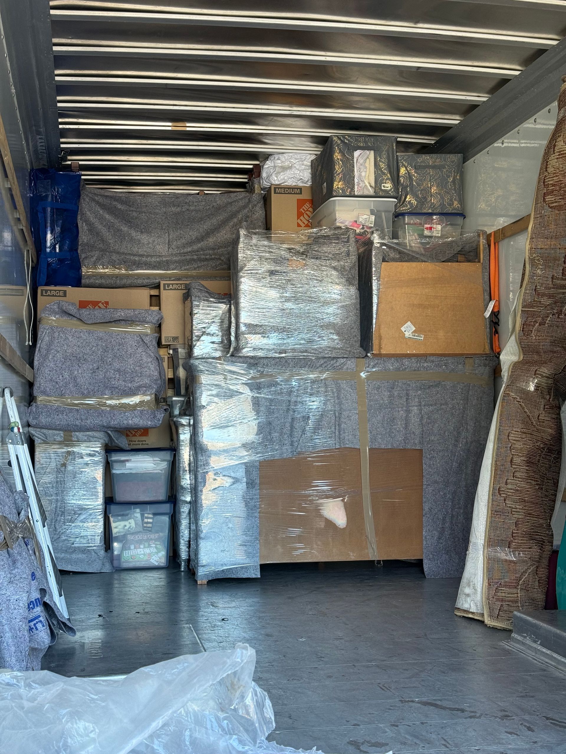 Packed moving truck interior with stacked boxes, furniture wrapped in plastic, and a large cardboard crate