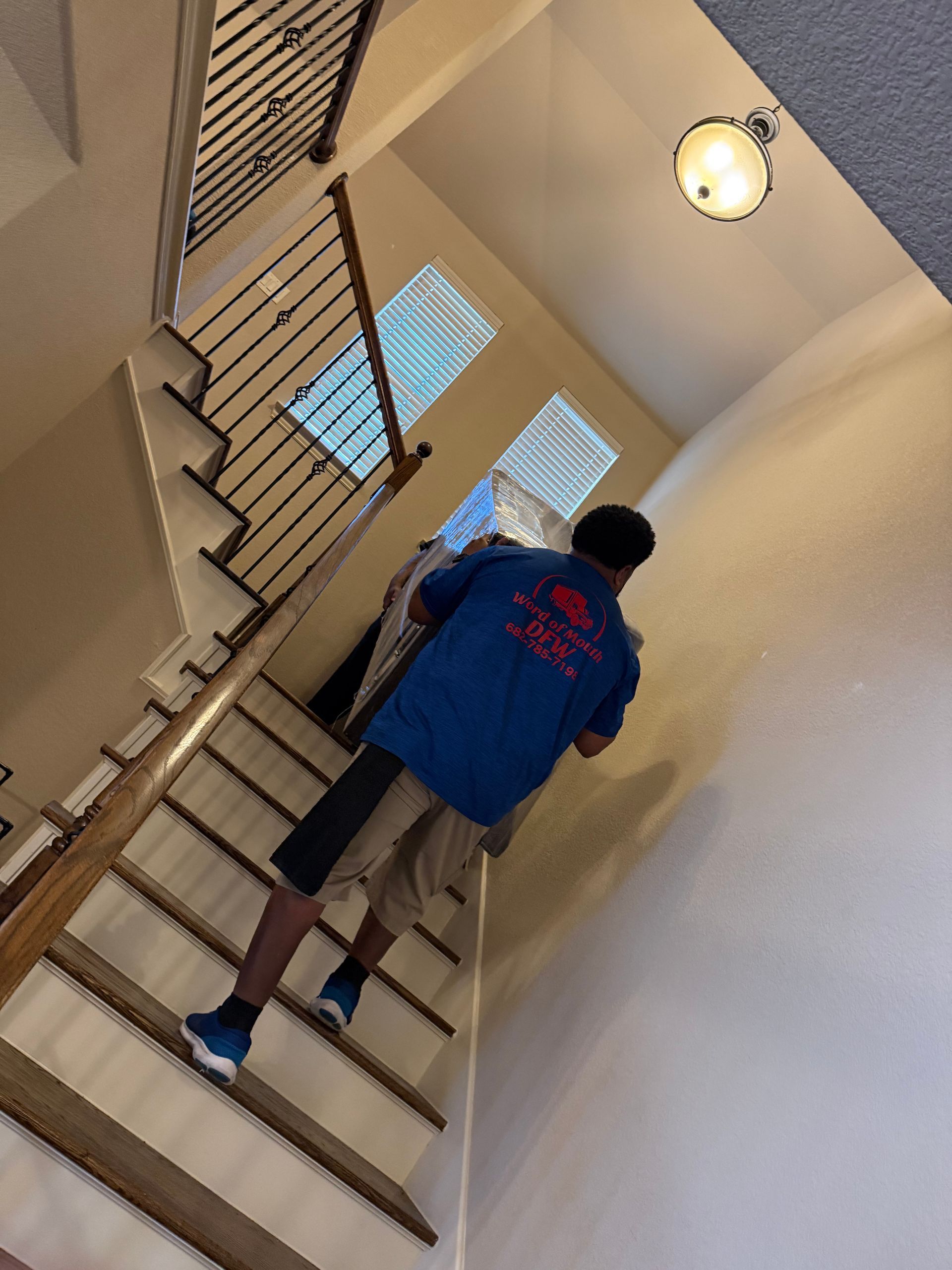 Person climbing an indoor staircase toward a bright landing, wearing a blue jacket and shorts.