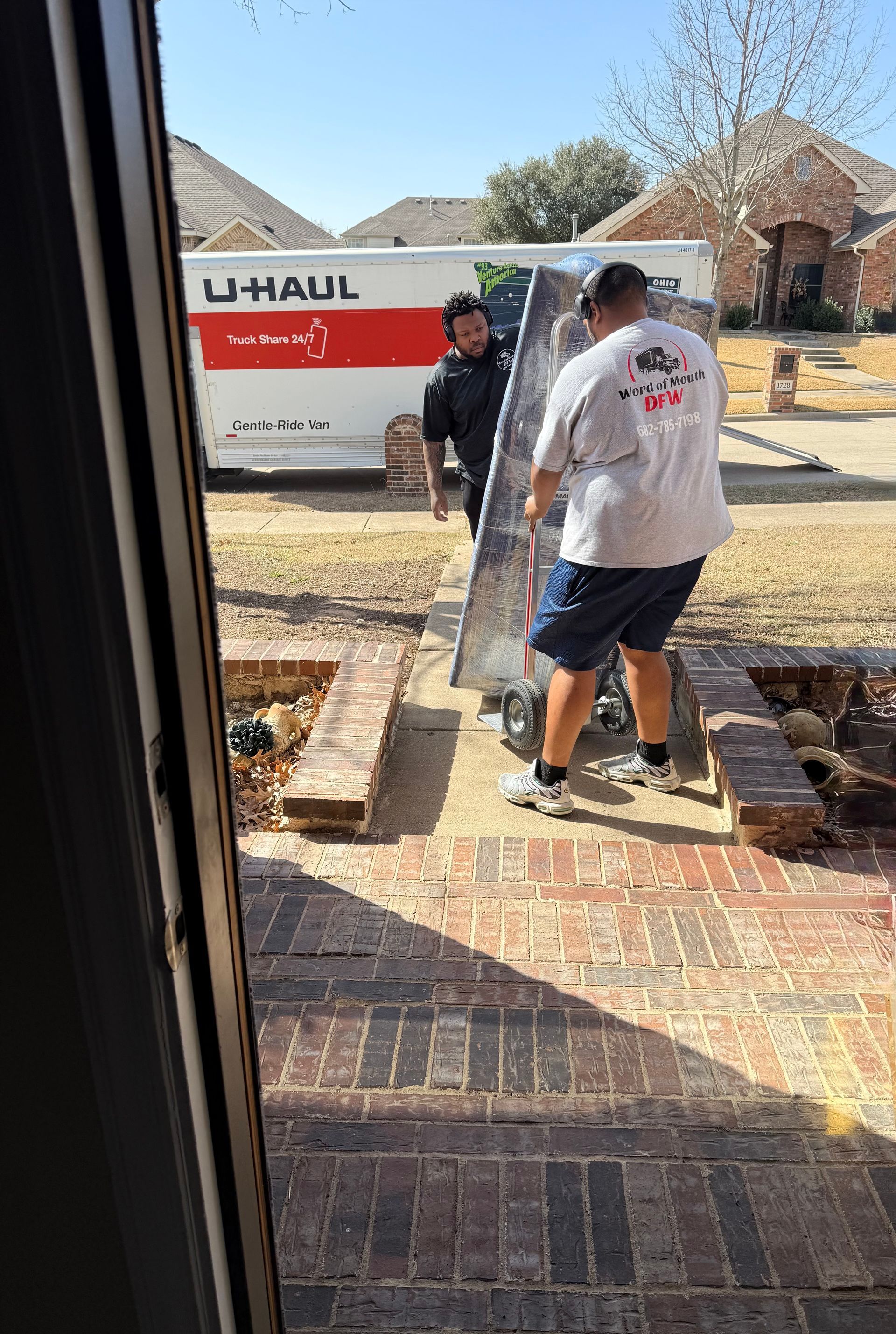 Two movers carrying a sofa toward a U-Haul truck along a brick walkway in a yard