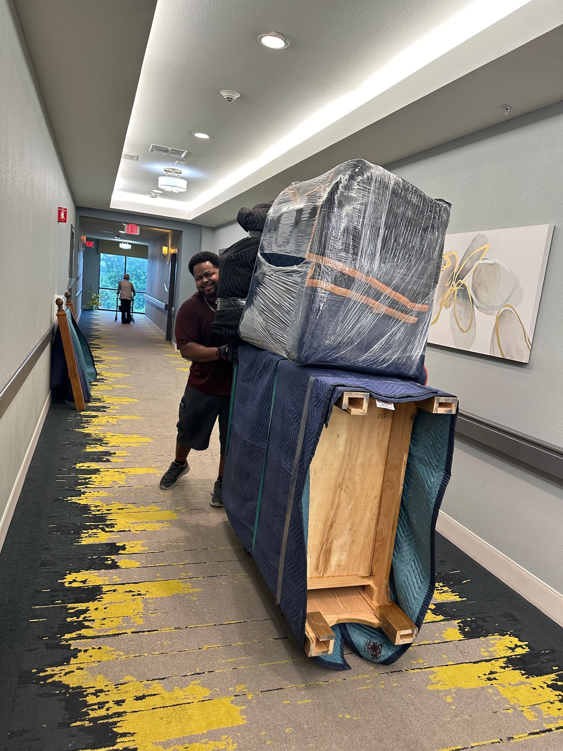 A man moves furniture wrapped in protective material down a hallway.