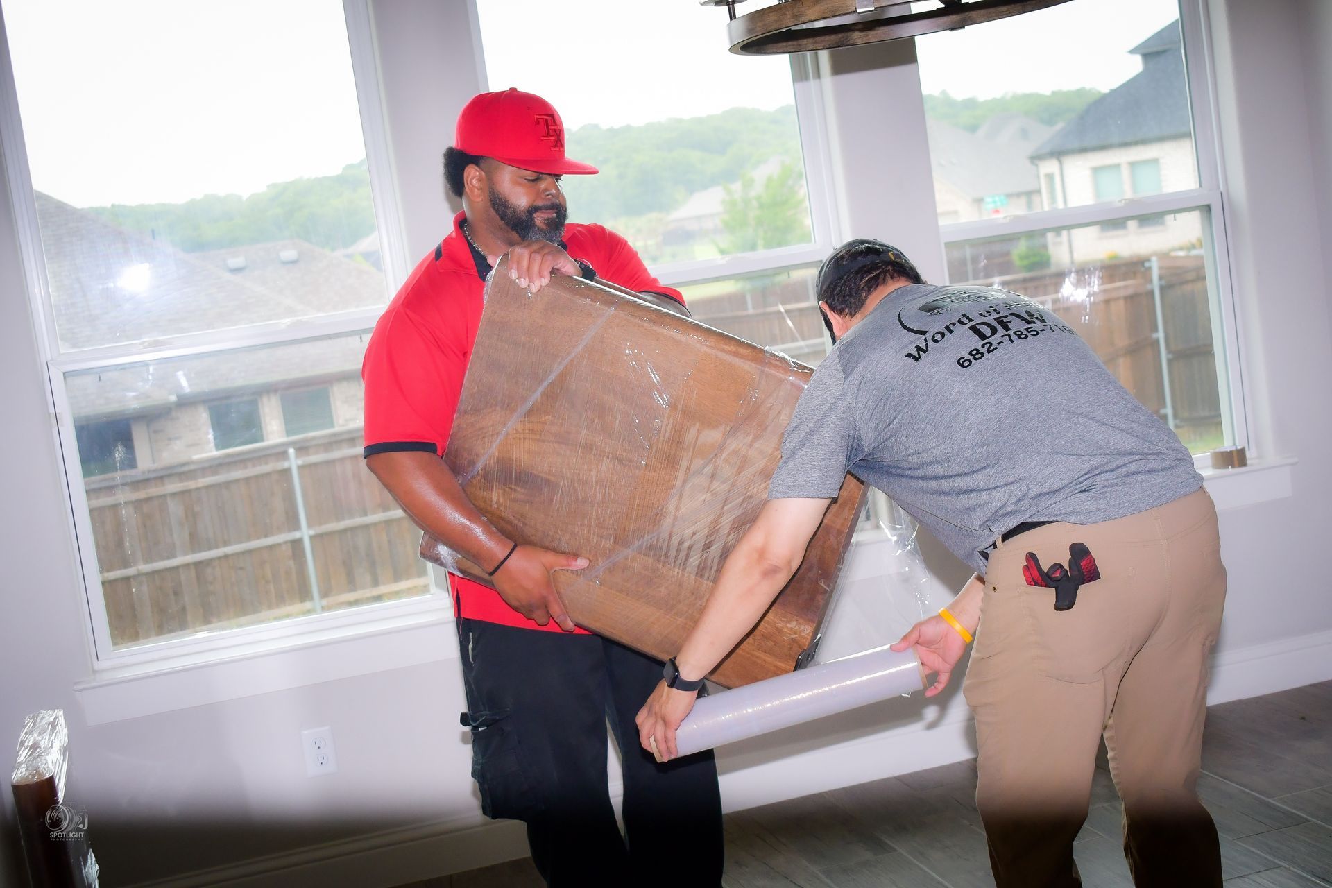 Two workers carrying a large box indoors near a window