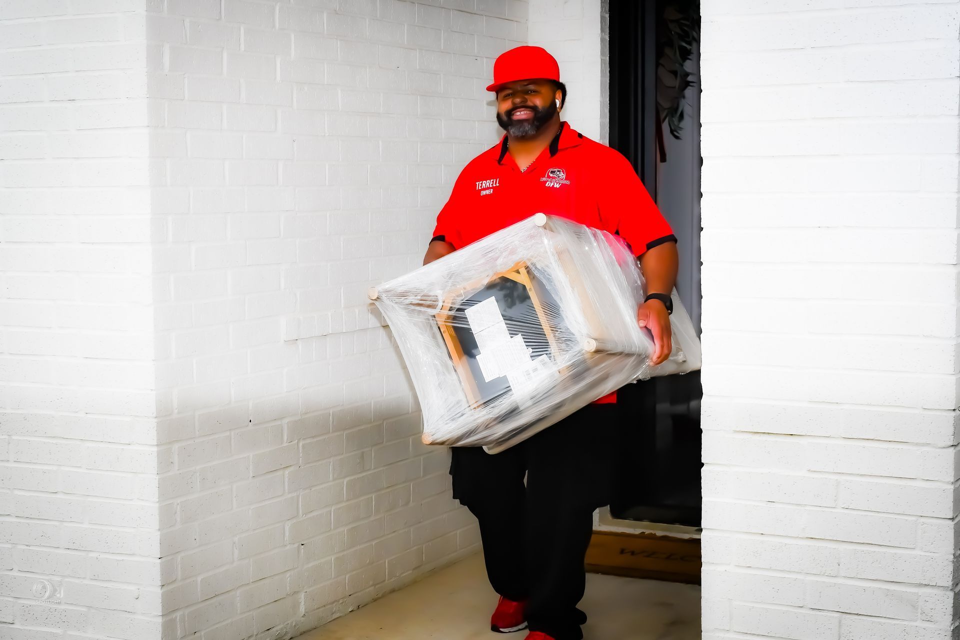 Delivery worker in red uniform carrying a large package through a doorway