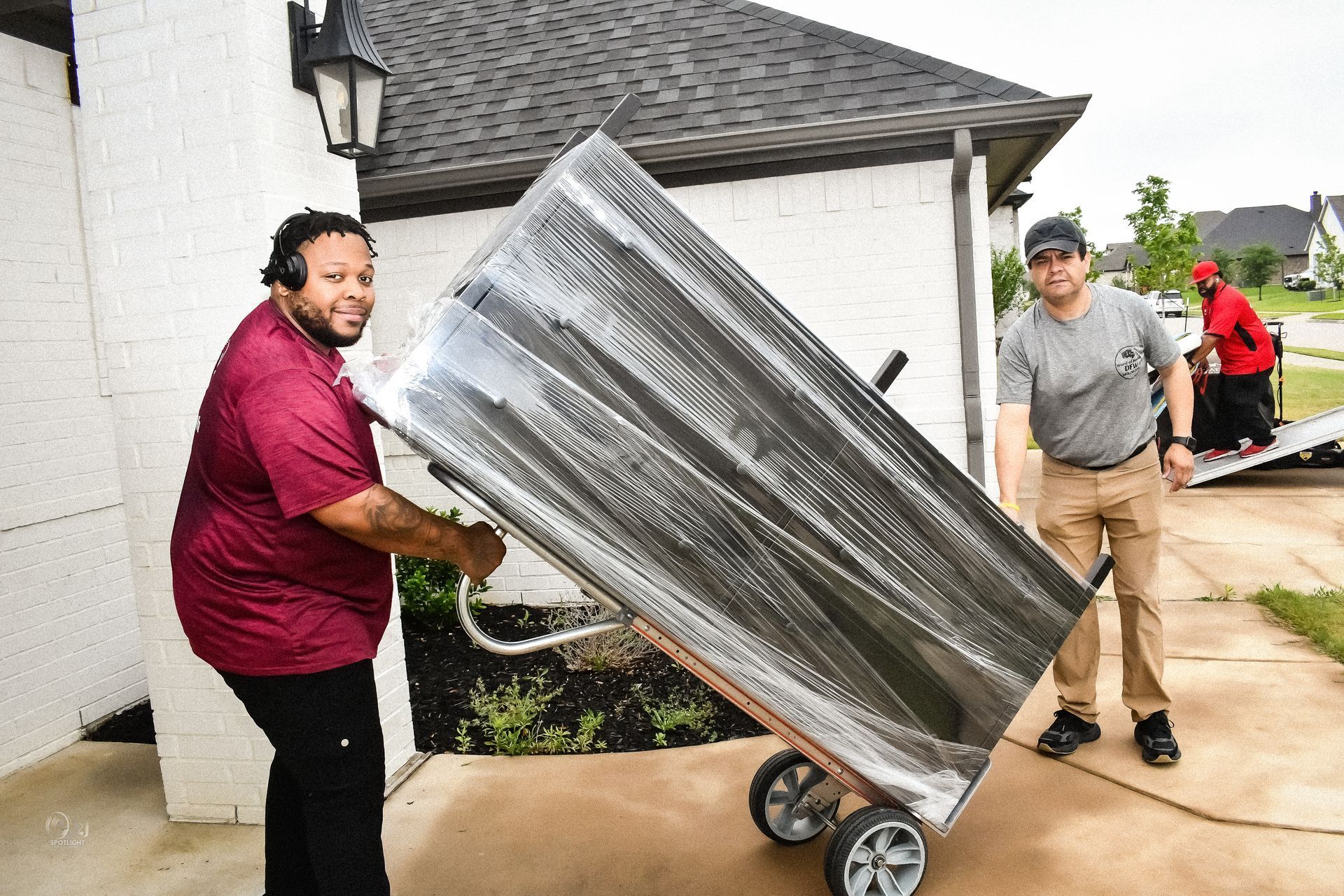 Two people moving a wrapped couch on a dolly near a house entrance