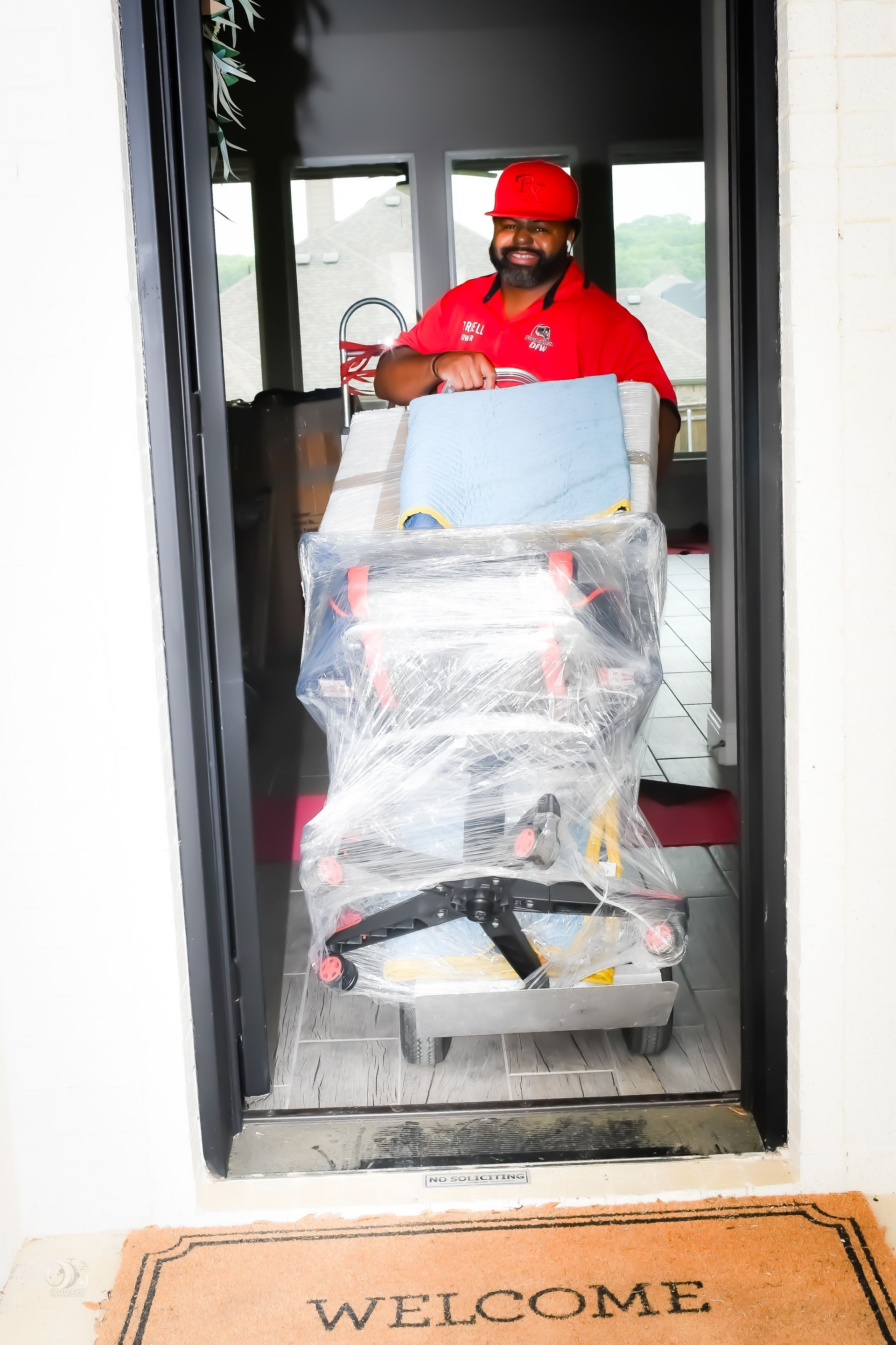 Delivery worker pushing a plastic-wrapped cart through a doorway onto a welcome mat