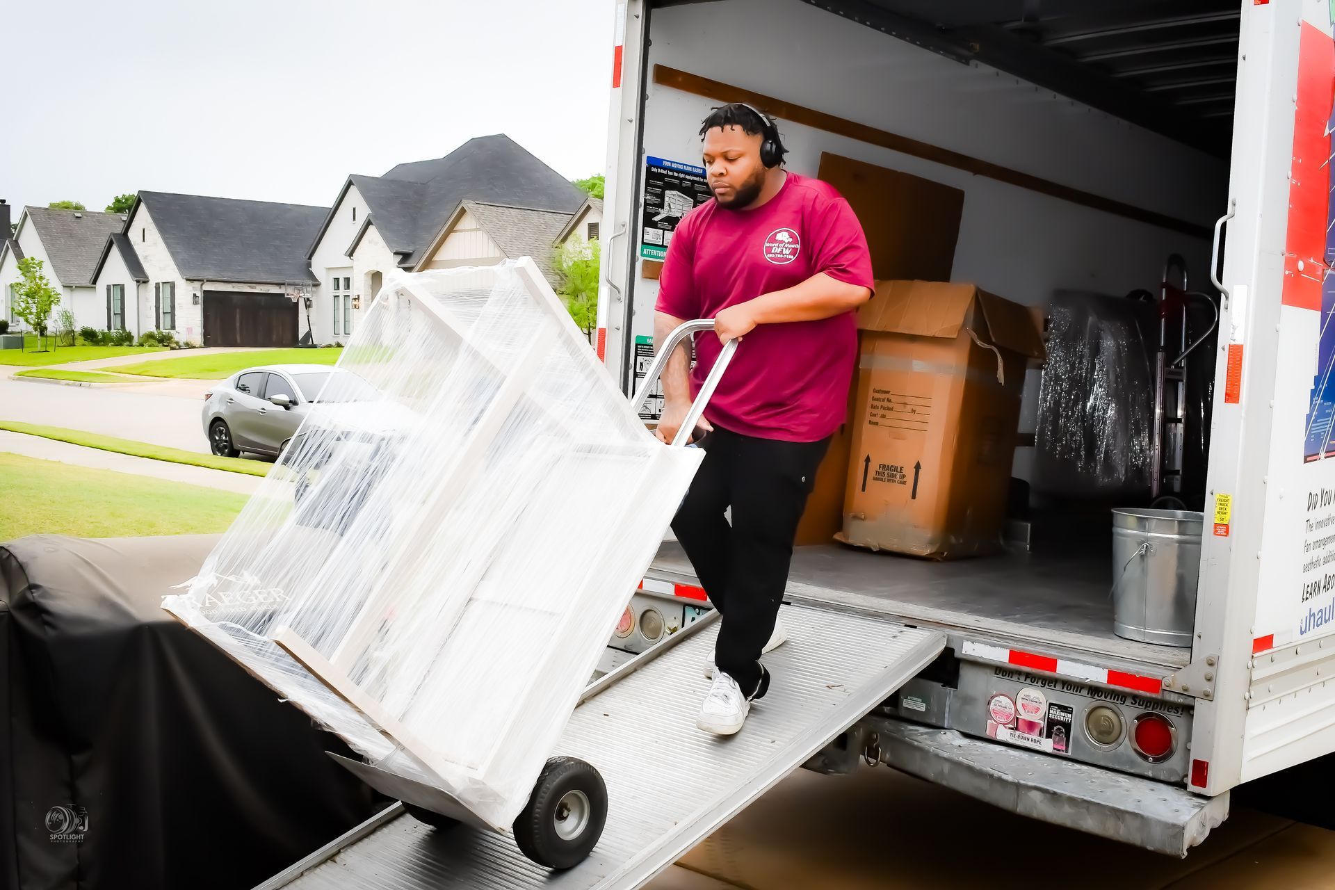 Mover unloading a wrapped cabinet from a moving truck onto a ramp in a suburban driveway