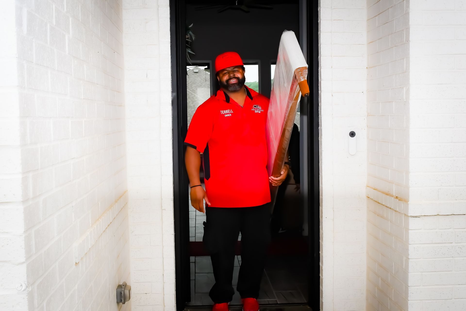 Person in a red shirt and cap stands in a narrow doorway holding a white board.
