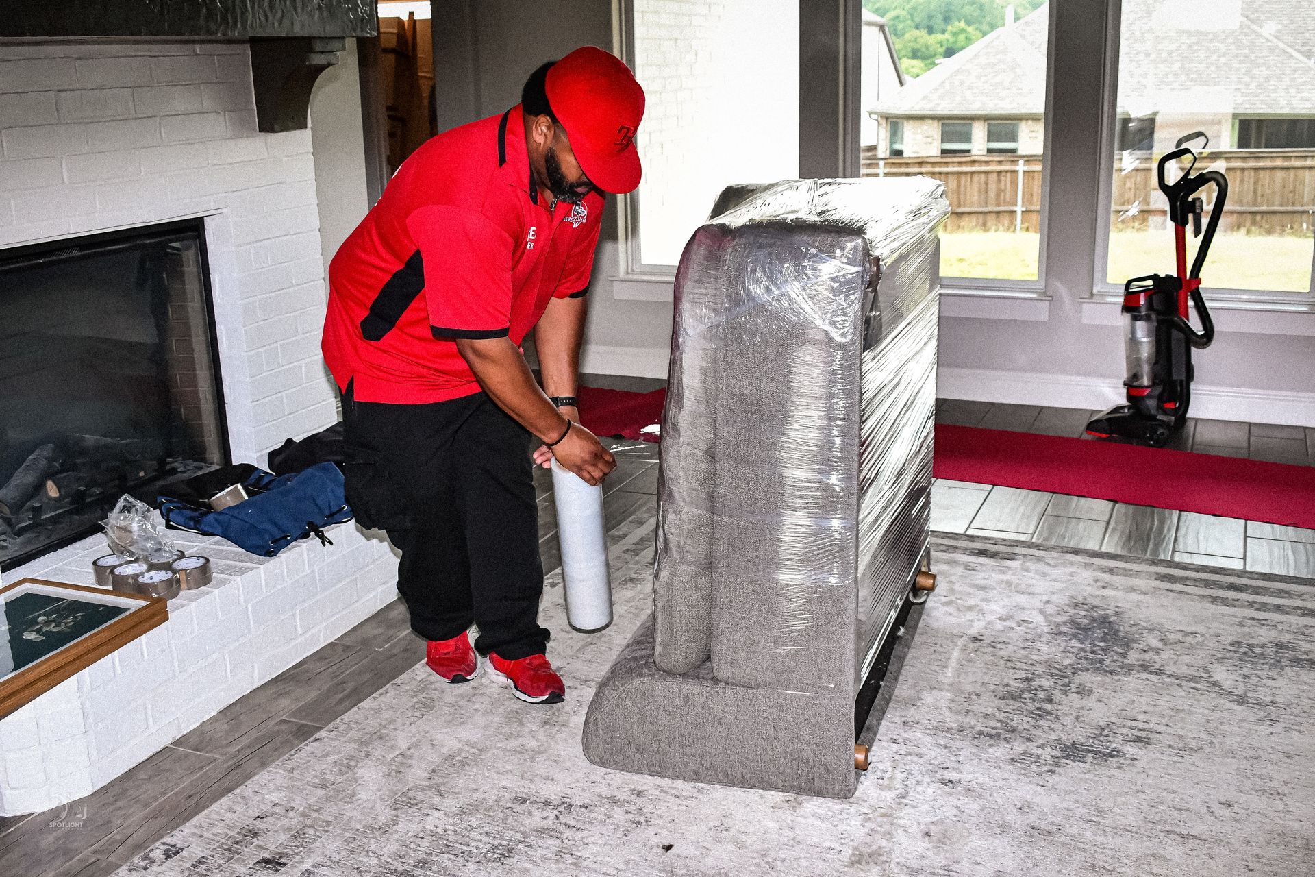 Worker in red uniform inspects a wrapped stone monument indoors with a spray can.