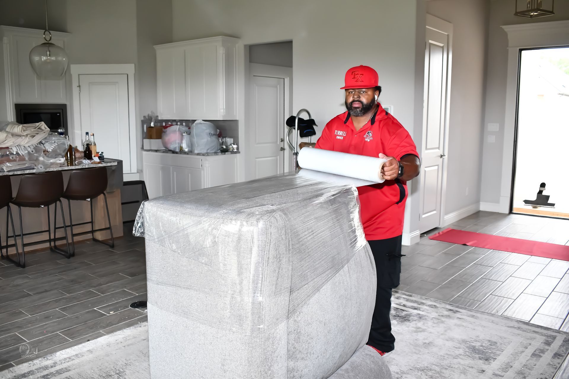 Mover in red shirt carrying a wrapped item through a bright living room