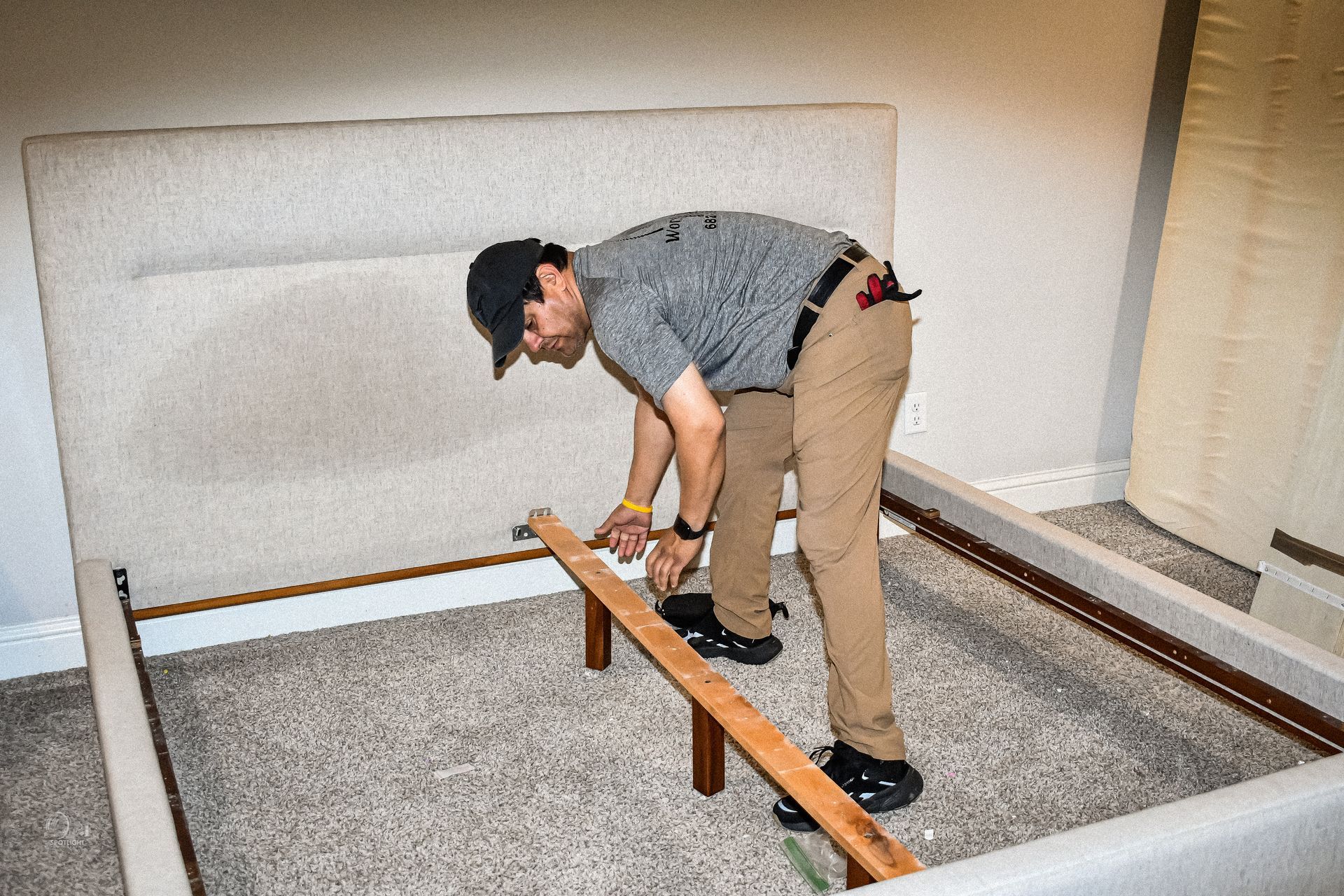 Person assembling a bed frame in a bedroom, using a tool on a wooden slat.