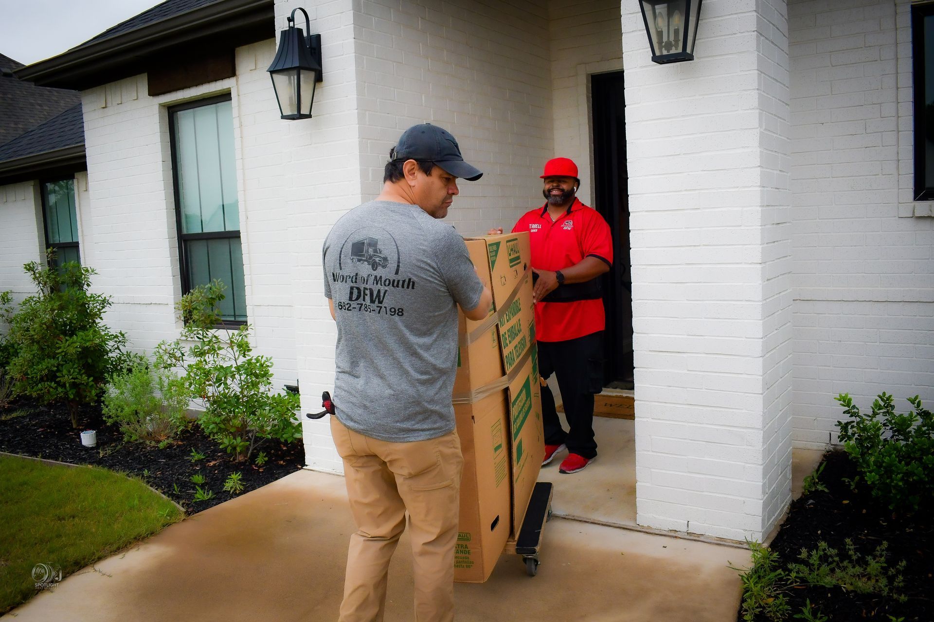 Two men moving a large box through a house doorway on a rainy front porch