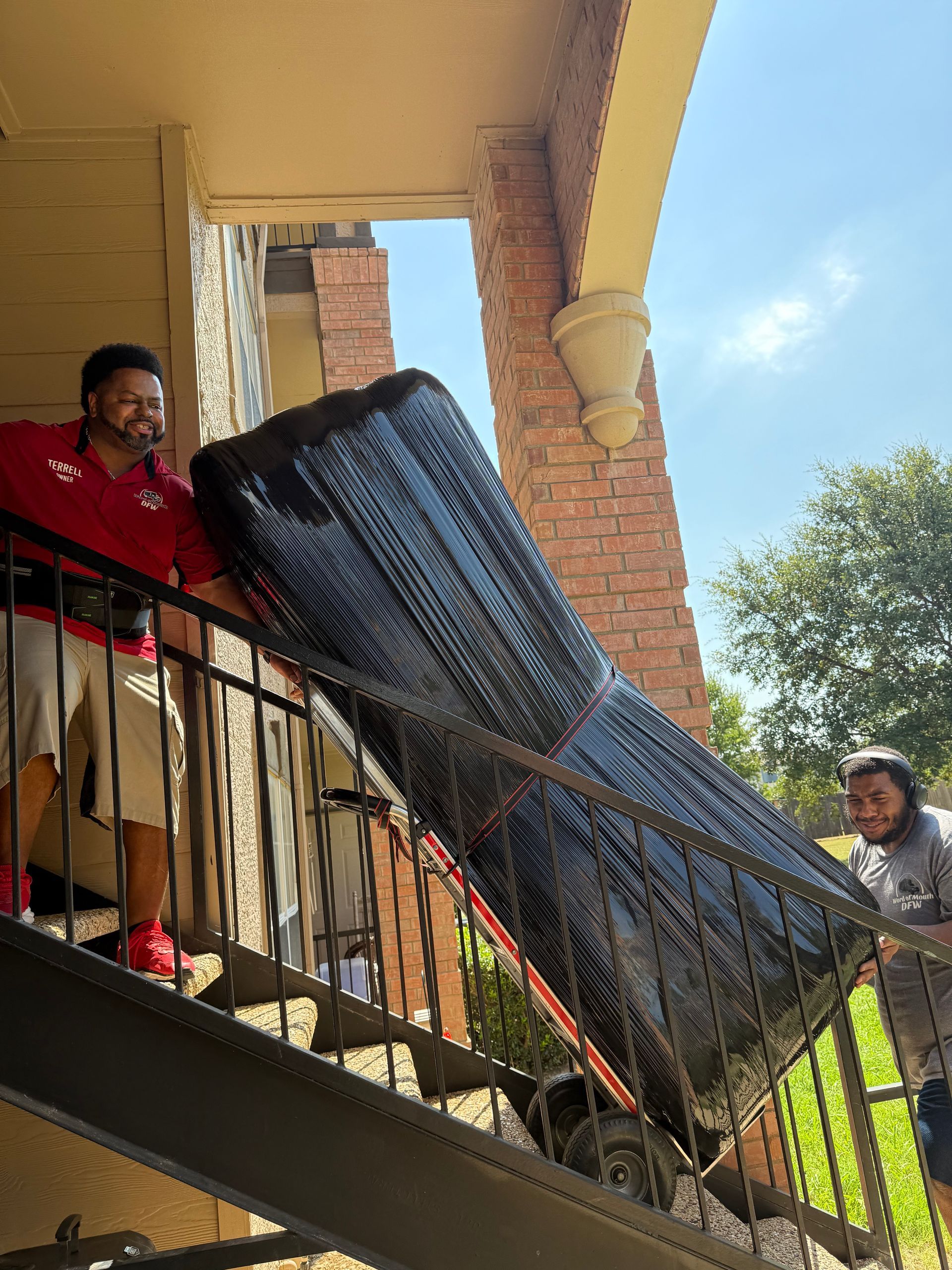 A man in a red shirt is carrying a mattress in a hallway.