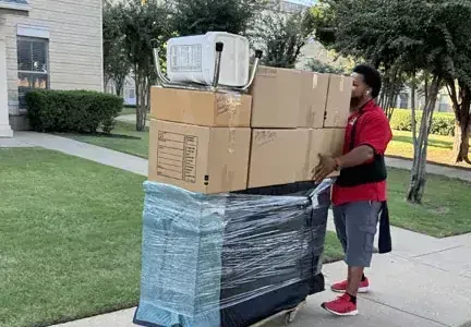A man is carrying a stack of boxes on a cart.