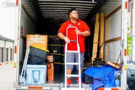 A man is standing on a ladder in the back of a moving truck.