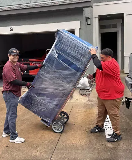 Two men are carrying a refrigerator on a cart.