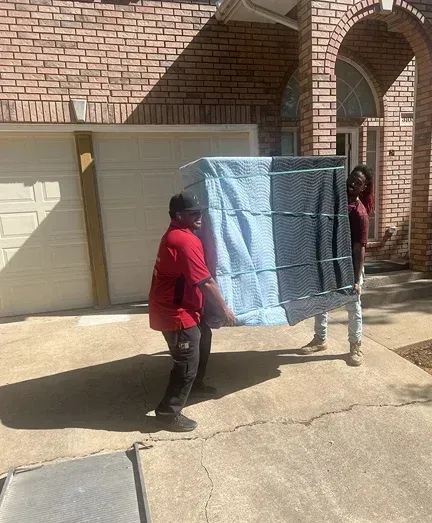 men are carrying a large box in front of a brick house.