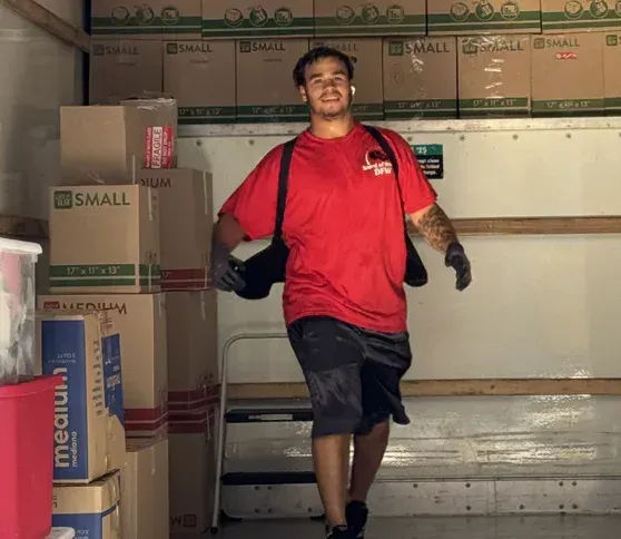 A man in a red shirt is standing in front of boxes that say small