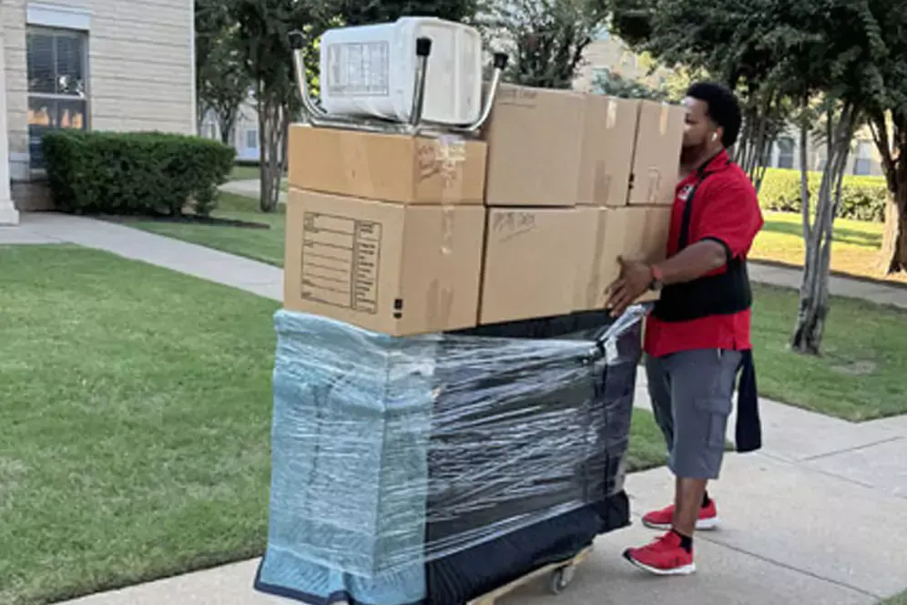 A man is carrying a stack of boxes on a dolly.
