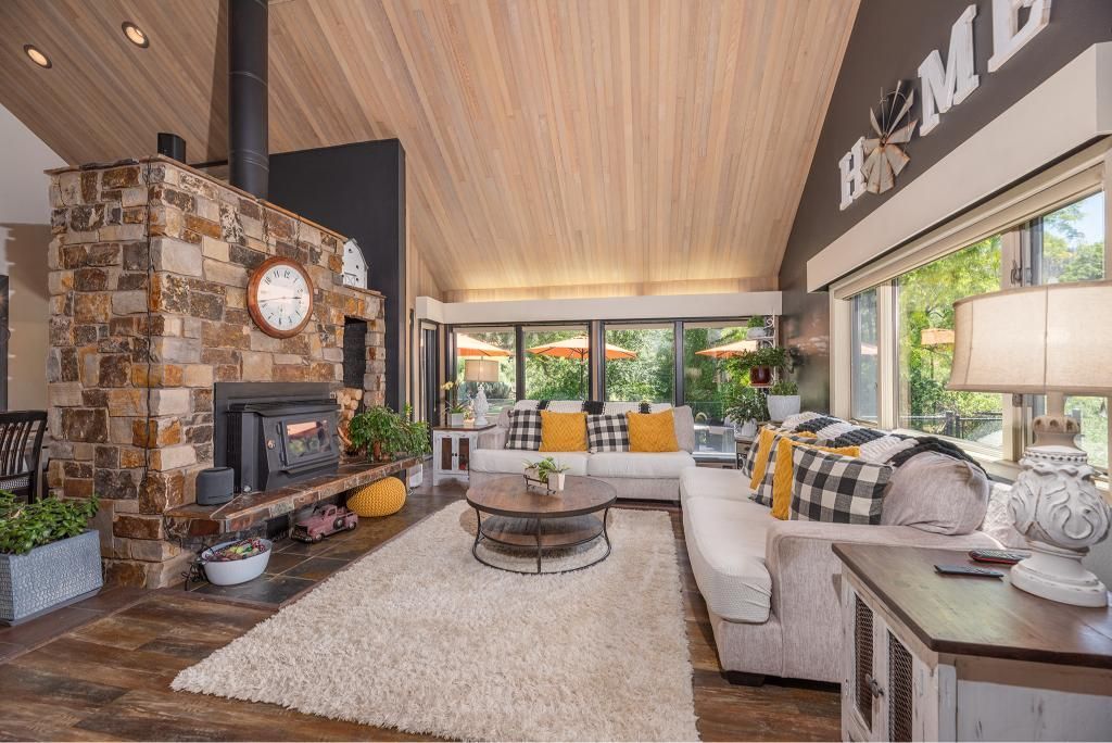 A cozy living room with a rustic stone fireplace, wood-paneled sloped ceiling, and a bright sofa with yellow accents.