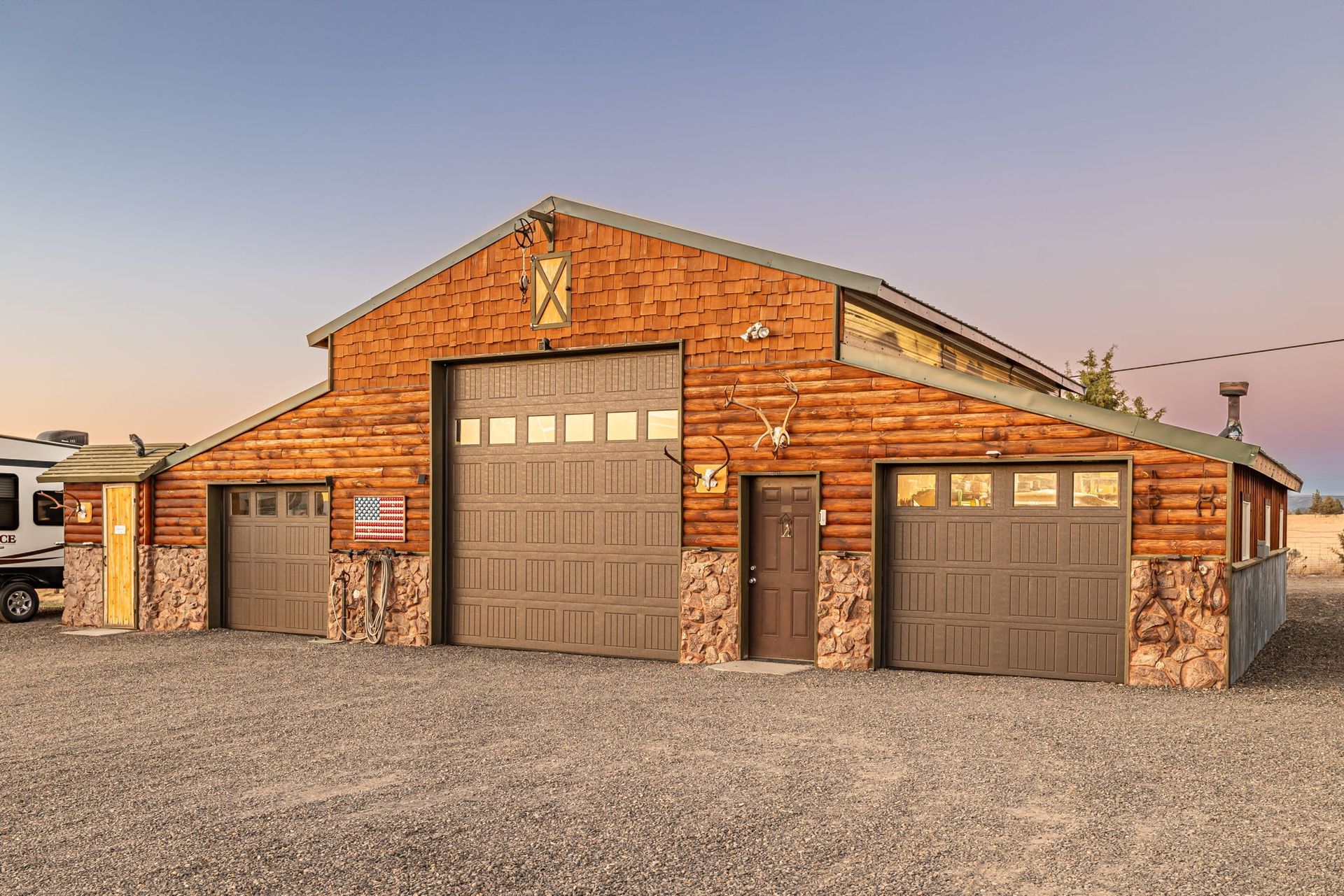 A rustic wooden barn-style garage with stone trim, featuring three garage doors and a central entrance door.