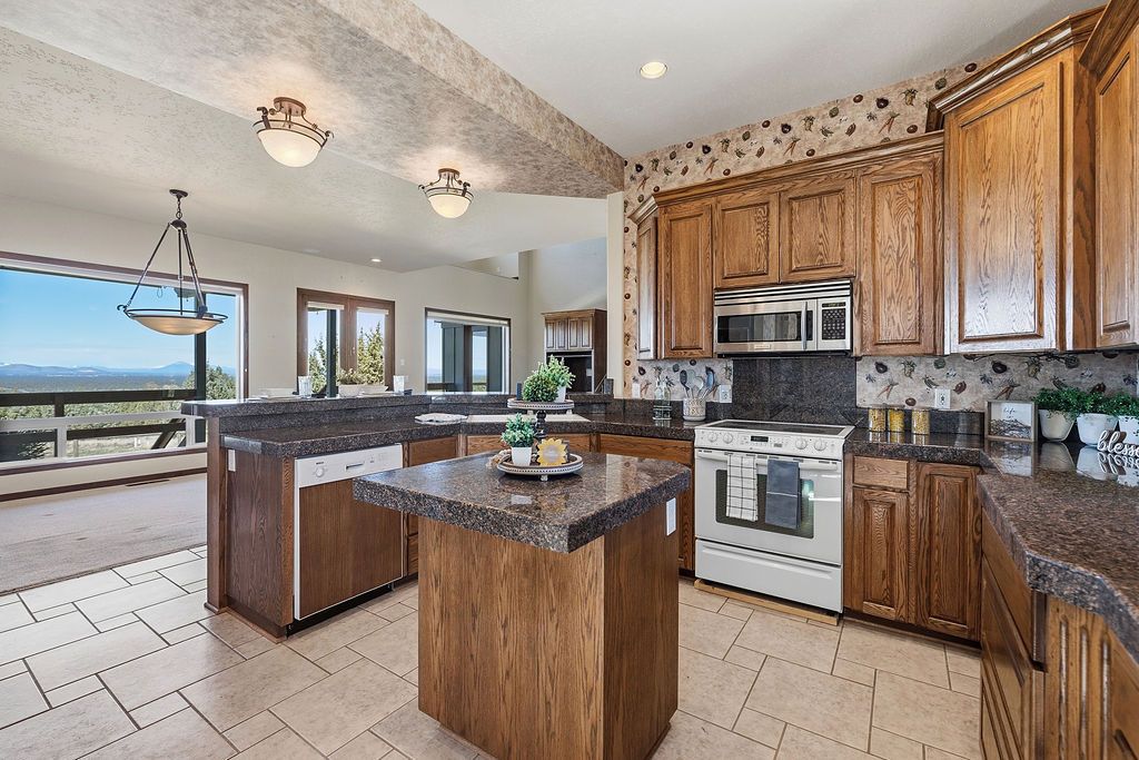 A kitchen featuring wooden cabinets, granite countertops, a center island, and a large window overlooking a landscape.
