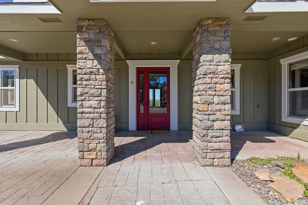 A front entrance with two stone pillars flanking a red door, set against a sage green exterior with paved walkway.