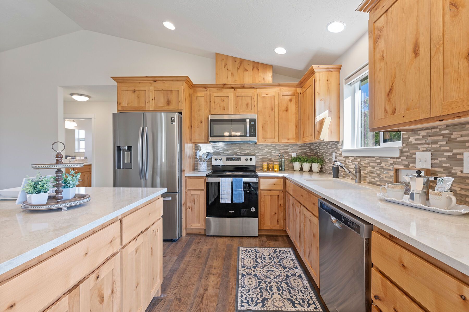 A well-lit kitchen features light wood cabinets, stainless steel appliances, a white countertop, and a tiled backsplash.