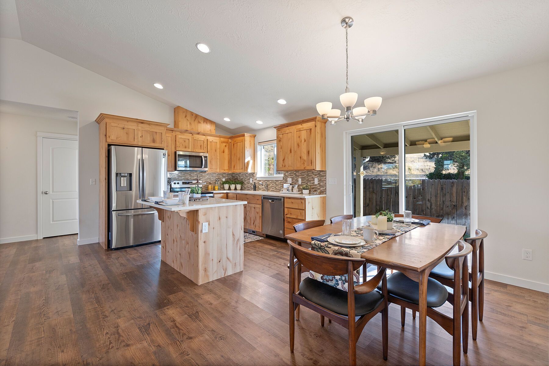 A bright, open-concept kitchen and dining area with wood cabinets, stainless appliances, and a wood-topped kitchen island.