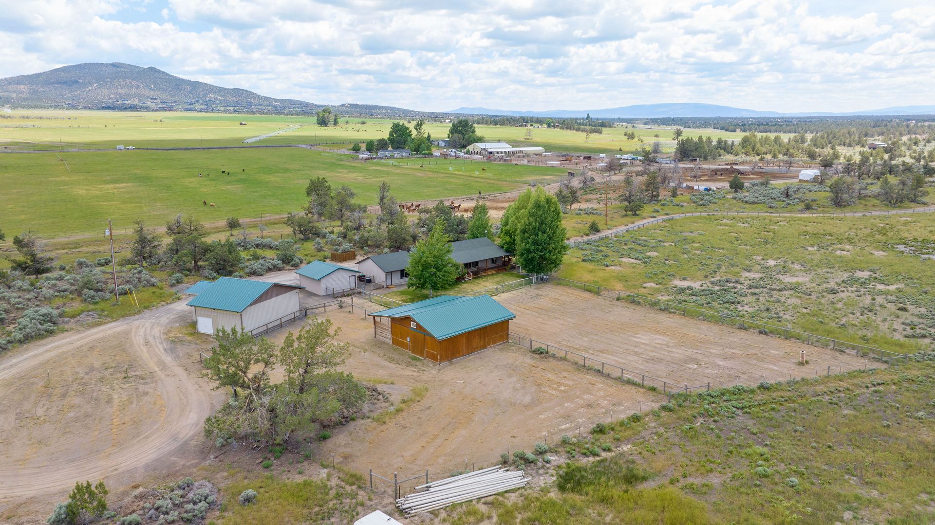 An aerial view of a property featuring several outbuildings with green roofs, set in a rural landscape near mountains.