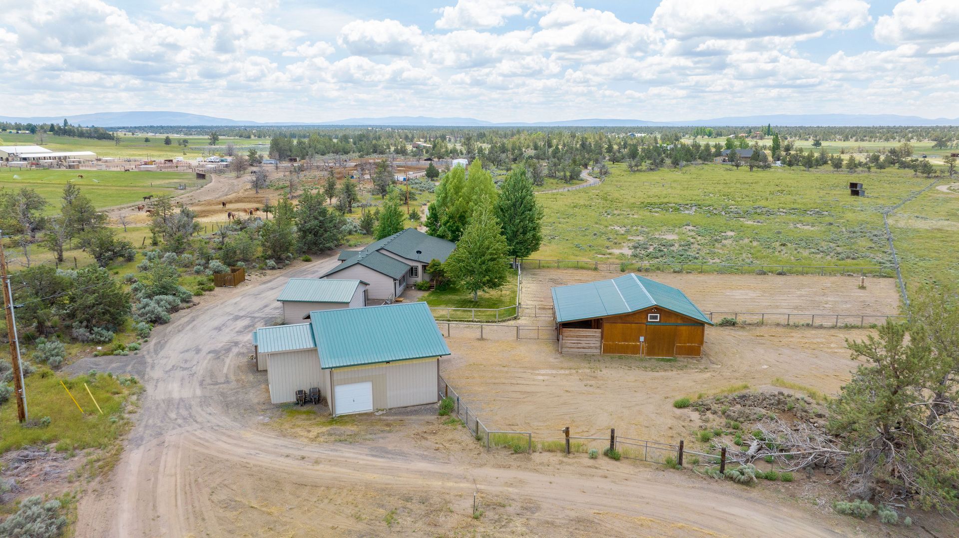 Aerial view of several rustic buildings with green roofs set on a rural property with dry fields and trees.