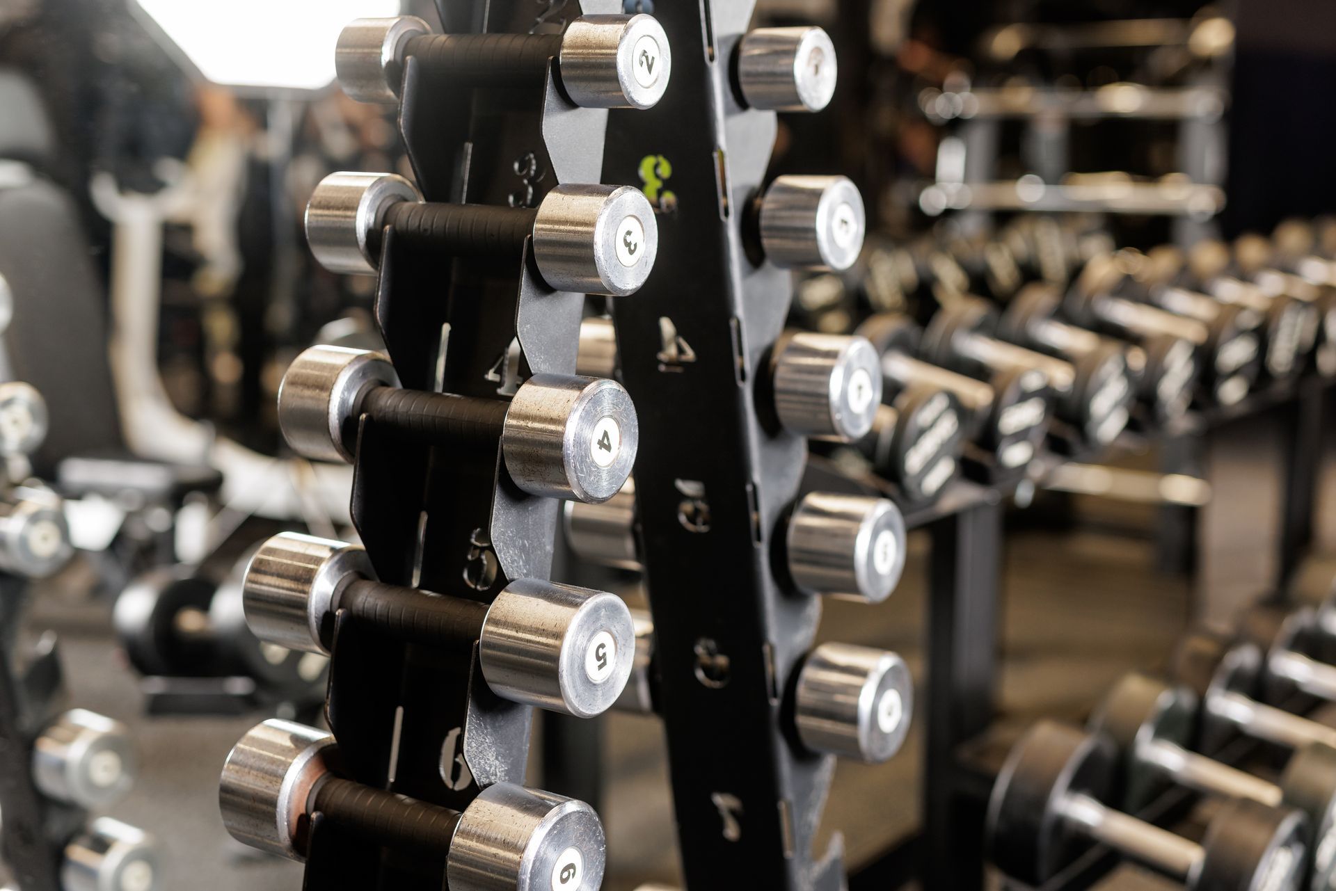 Rows of polished chrome dumbbells resting on tiered black steel racks in a fitness equipment store.