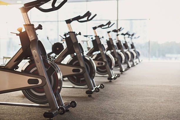 Row of stationary exercise bikes in modern fitness gym with large windows and natural light.