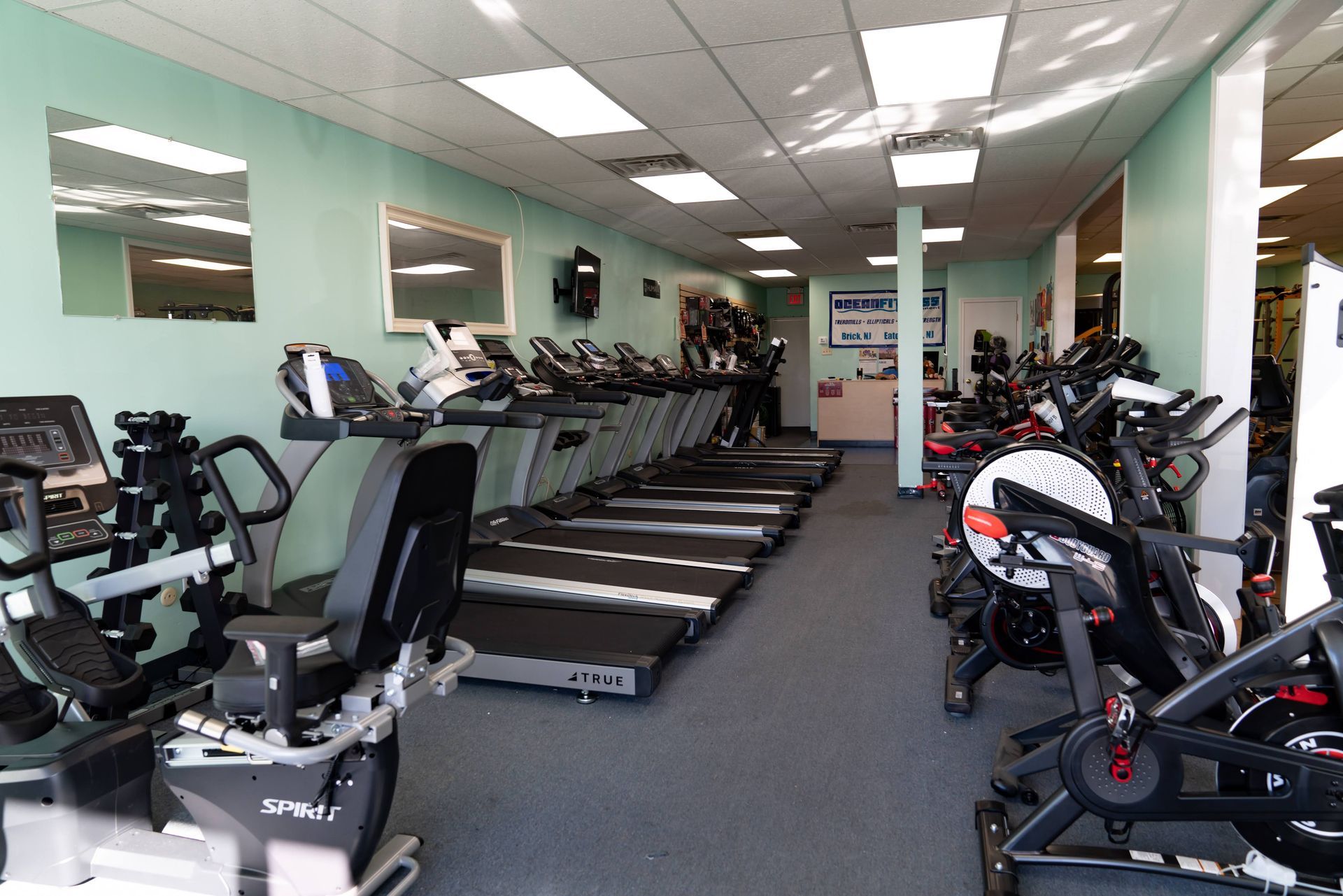 A fitness center with multiple treadmills lined up, stationary bikes on the right, and mint green walls.