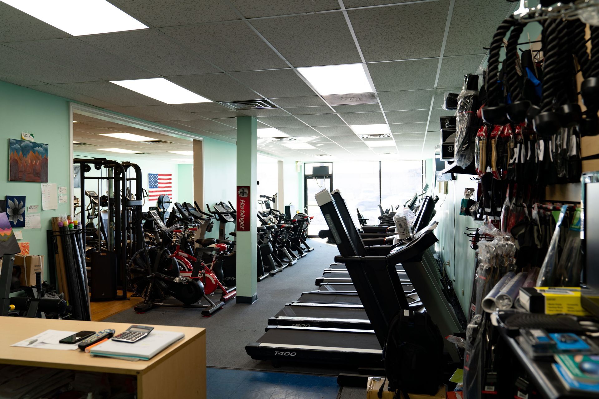 Interior view of a gym featuring a row of treadmills, stationary bikes, exercise equipment, and a front desk area.