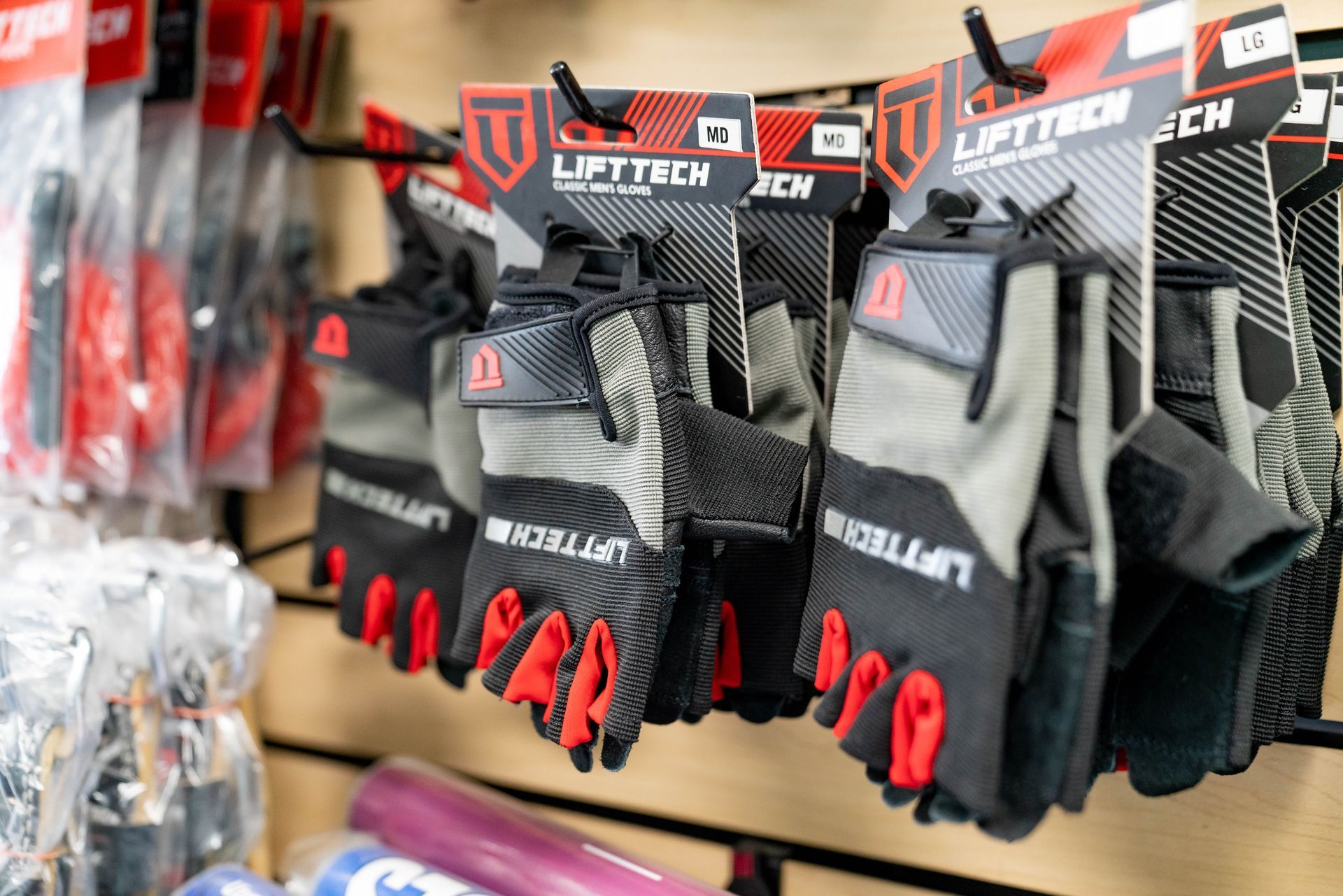 Pairs of black and red LiftTech weightlifting gloves hanging on a retail display rack.