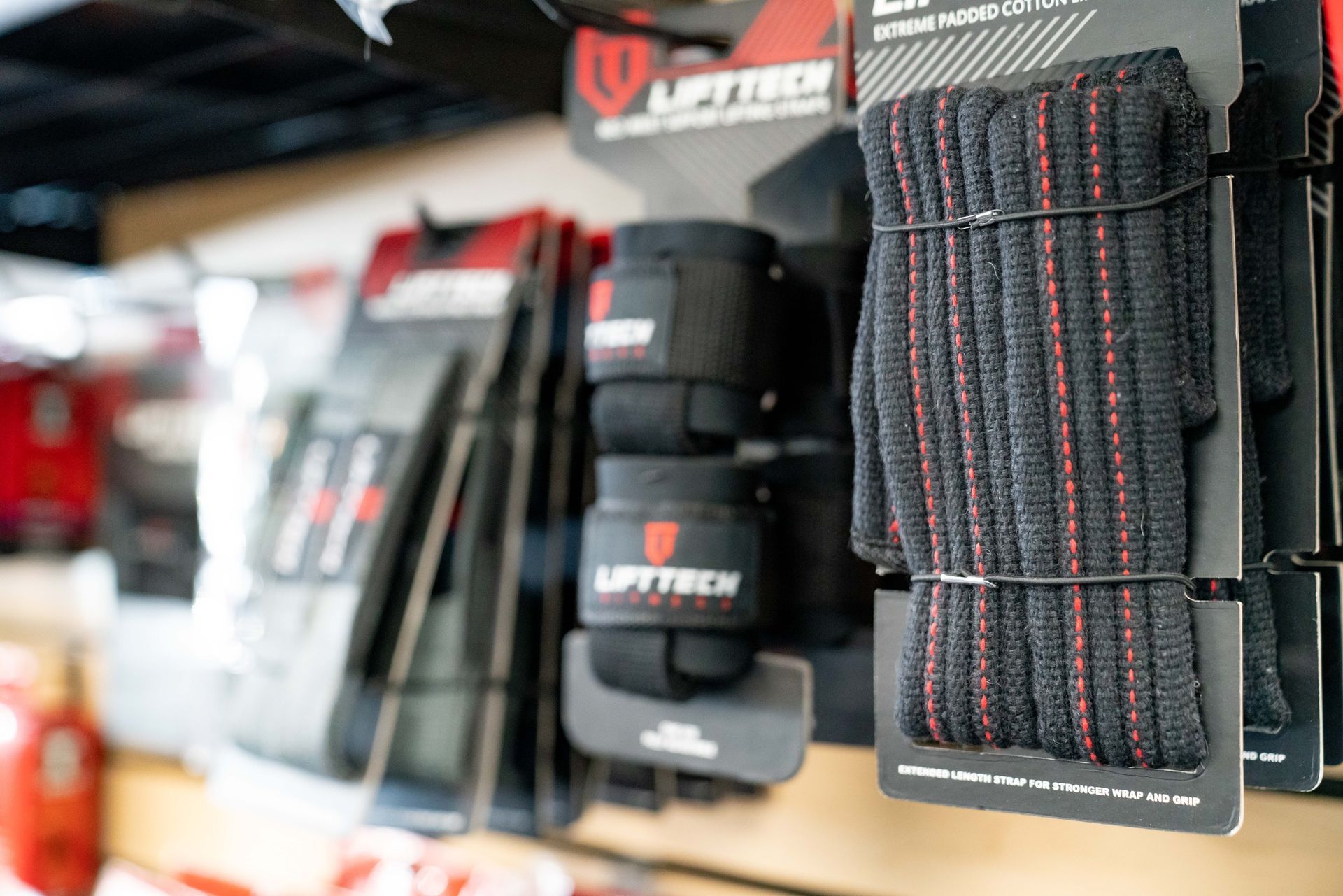 Wrist wraps for weightlifting, featuring black elastic with red stripes, displayed on store shelves.