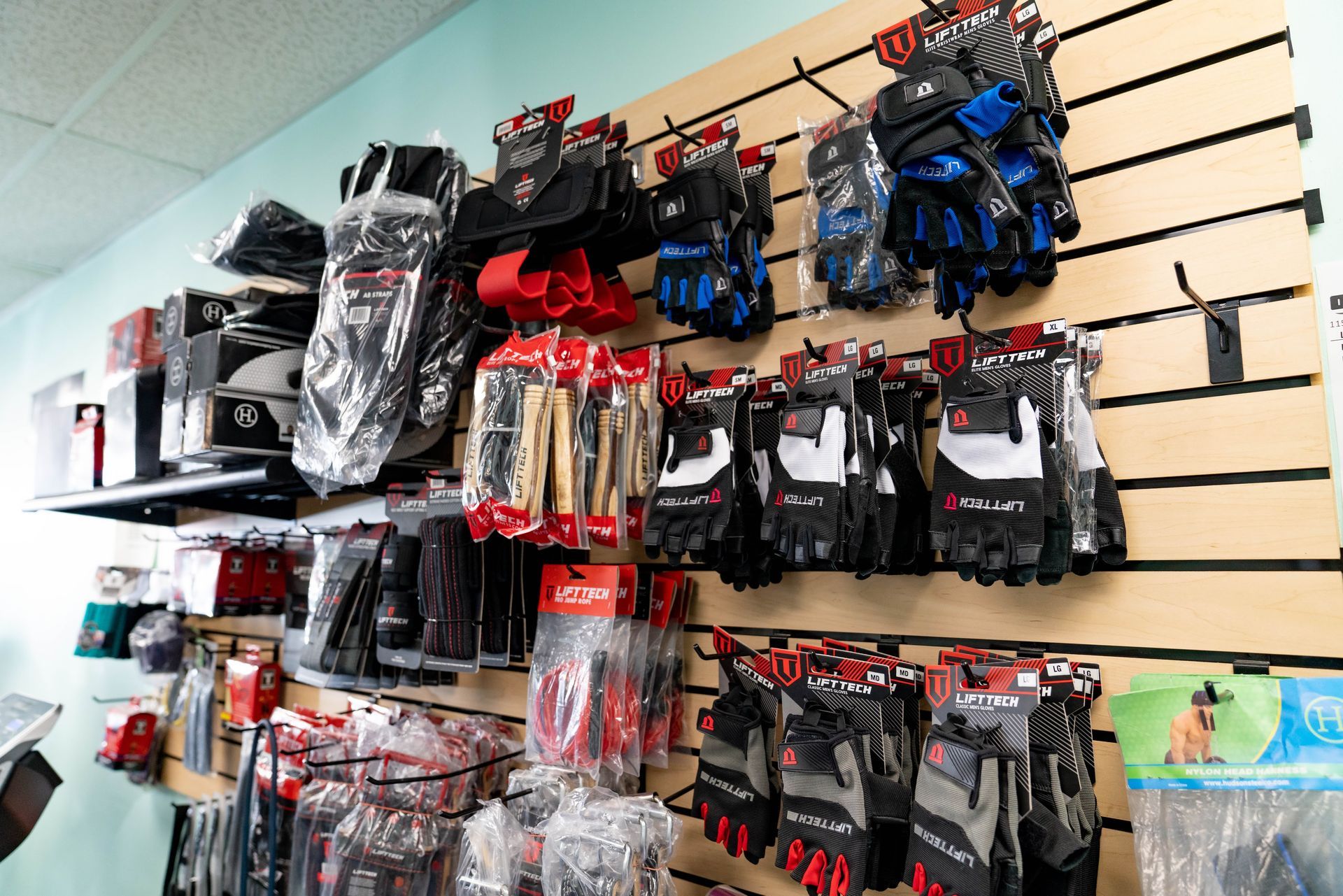 Retail wall display featuring various pairs of packaged work gloves in black, red, blue, white, and gray.