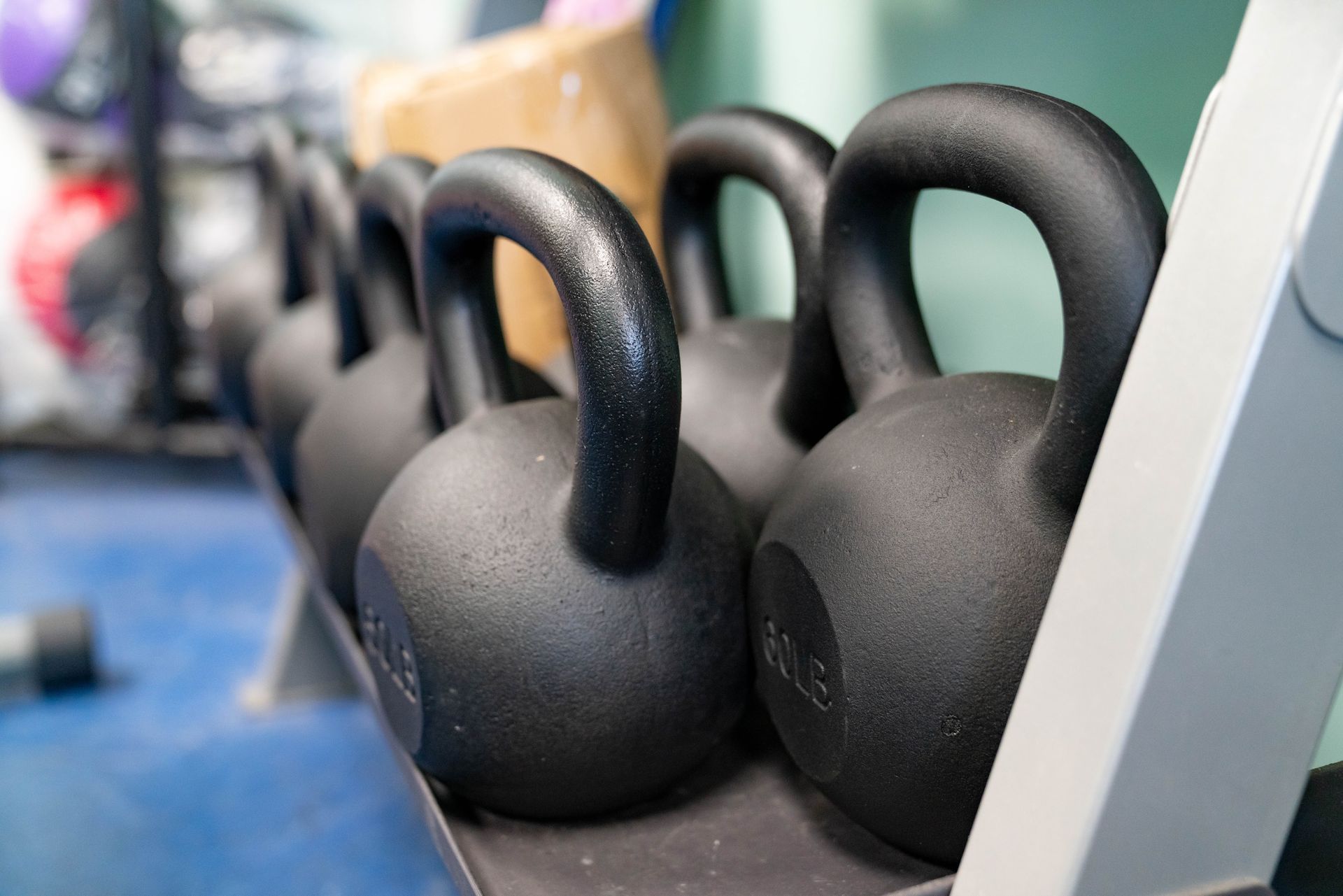 A row of black kettlebells resting on a storage rack in a gym.