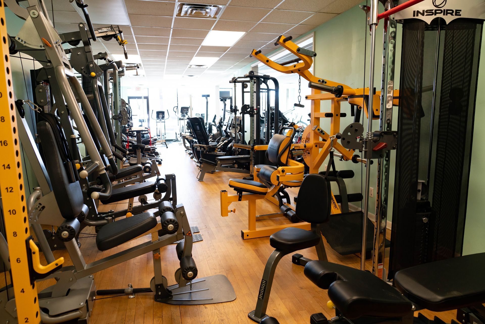 A view of a gym interior with various weight training machines arranged along a wooden floor.