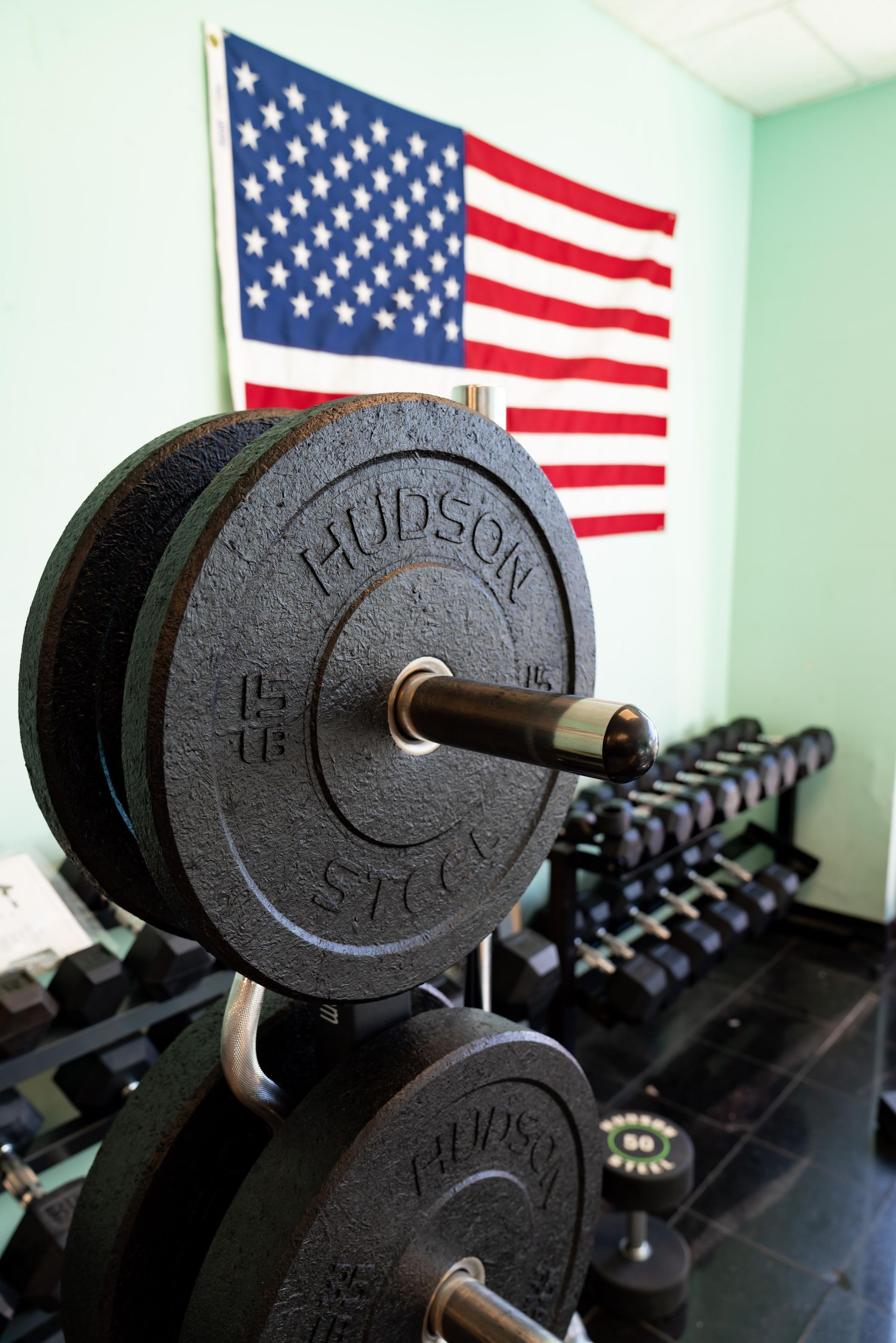 Black weight plates on a rack in a gym with an American flag hanging on the wall in the background.
