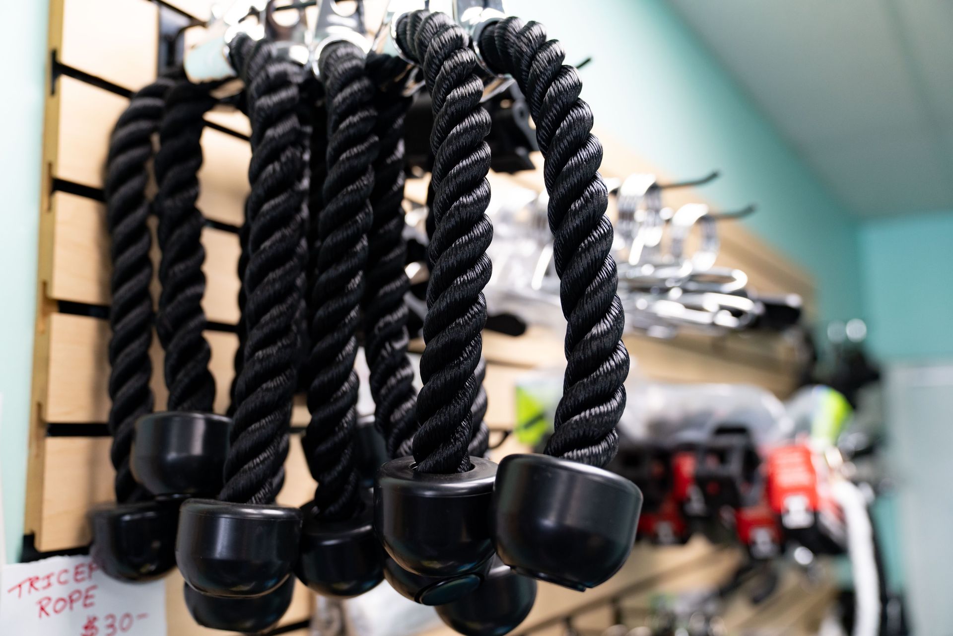 Several black tricep ropes with rubber end caps hanging on a slat wall display in a gym or store.