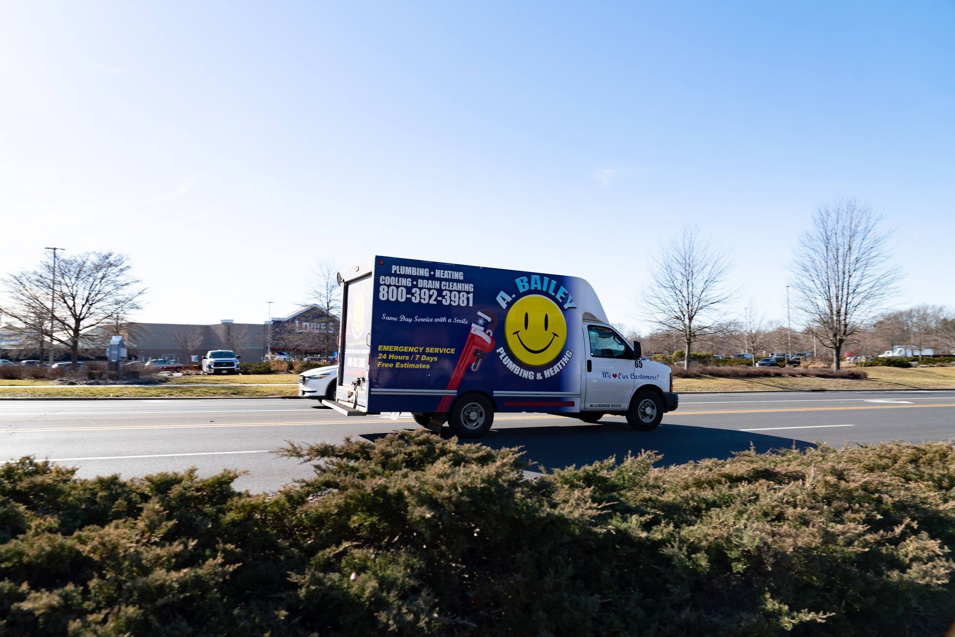 A blue and white box truck with a yellow smiley face logo drives across a parking lot under a clear blue sky.